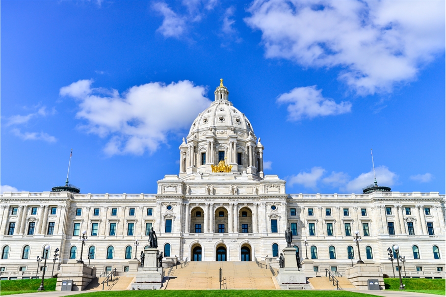 [ai] The Minnesota State Capitol building, featuring its grand dome topped with a golden statue, set against a blue sky with clouds. The facade is made of light-colored stone, with large columns and walkways leading to the entrance.